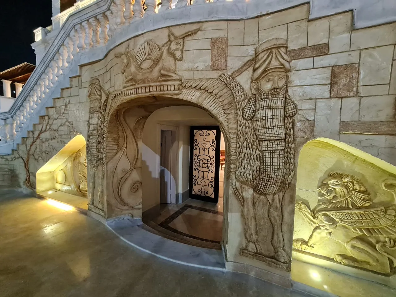 A lower entrance framed by relief decoration and warm lighting beneath the stairs