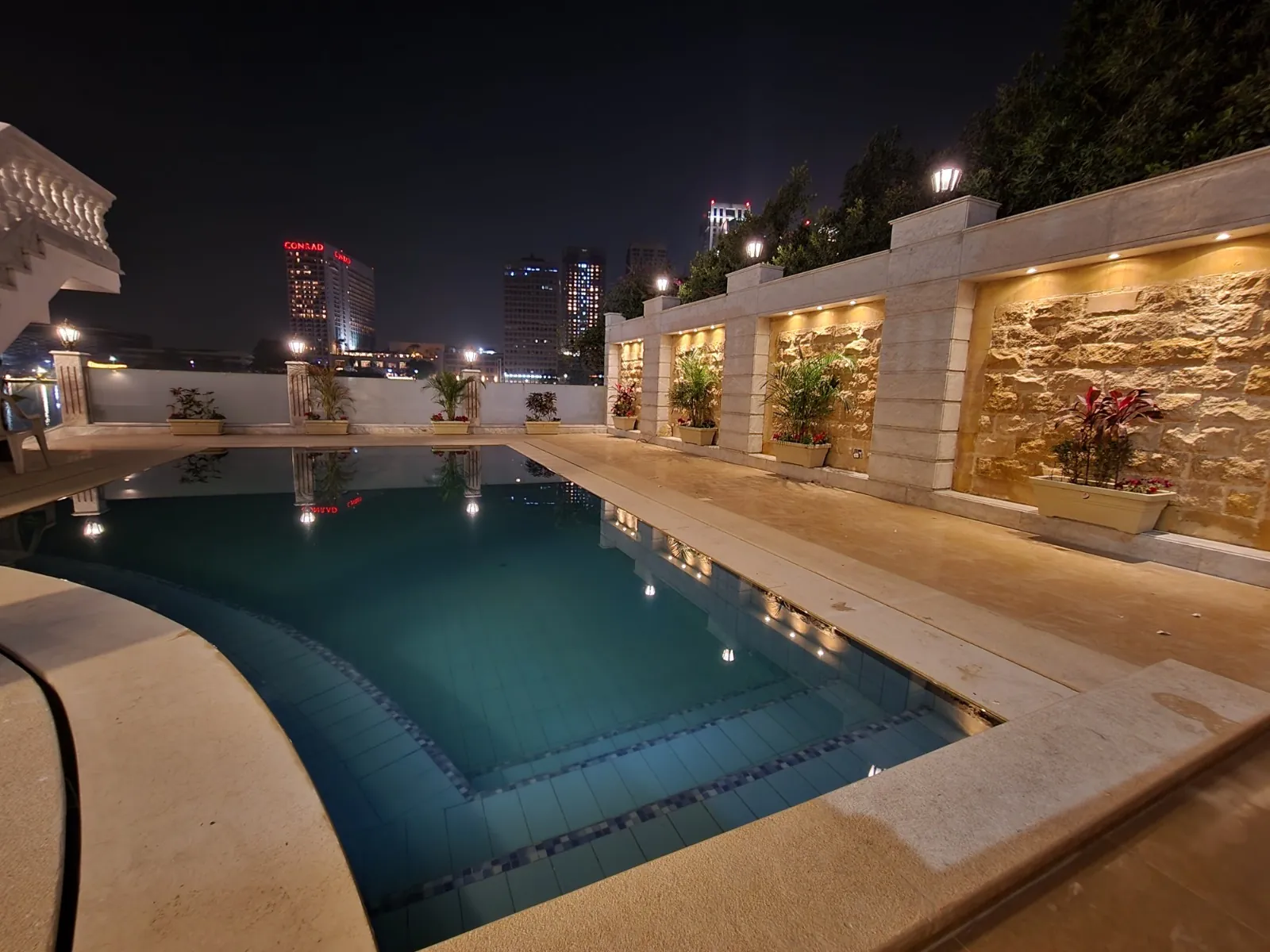 The outdoor pool at night, bordered by an illuminated wall and planting details