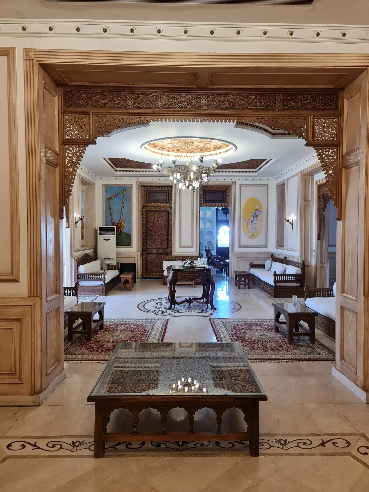 A sequence of interior rooms seen through a broad decorative opening, with a bordered floor pattern