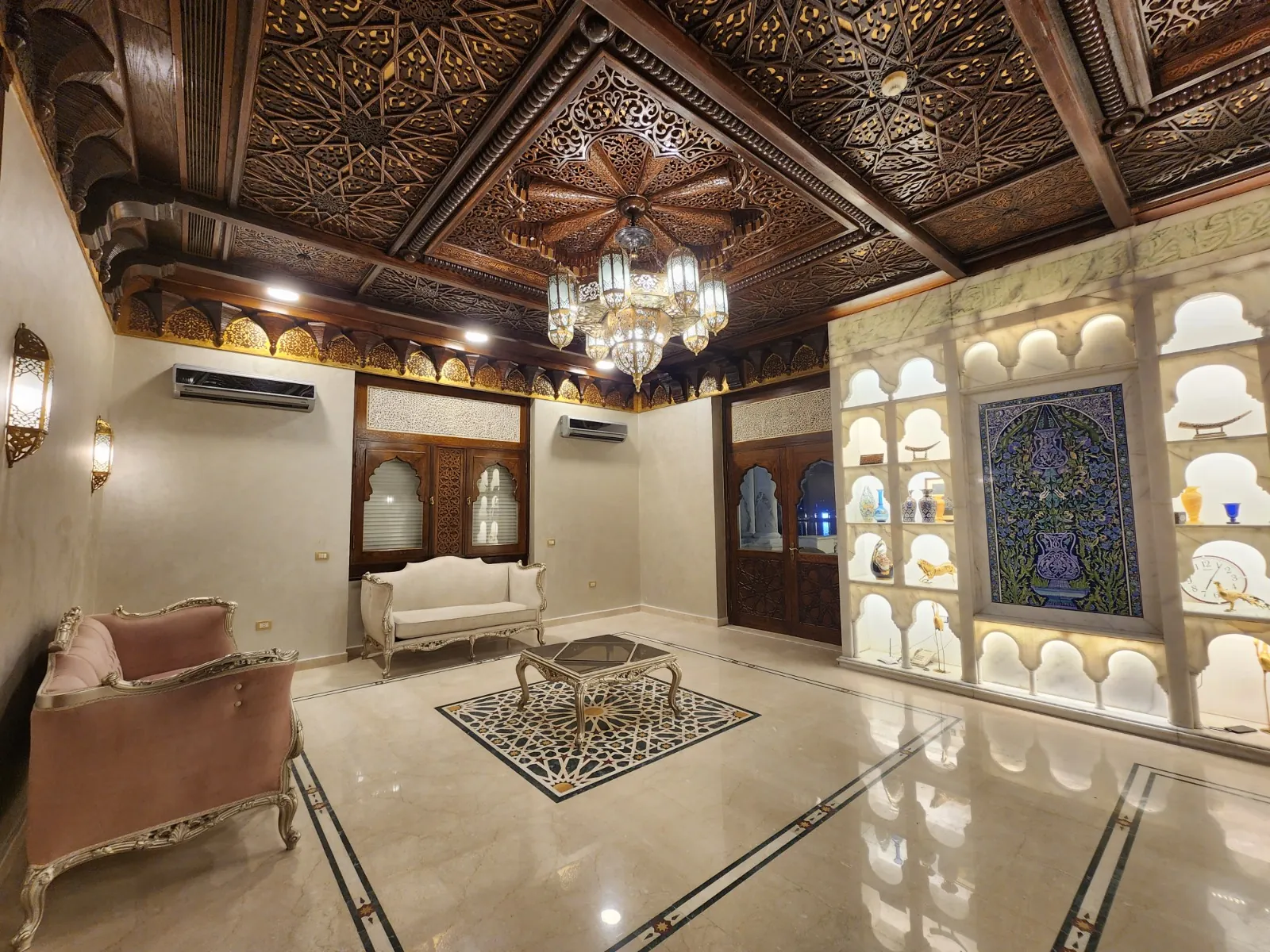A sitting room with an ornate dark ceiling, chandelier and illuminated wall display niches
