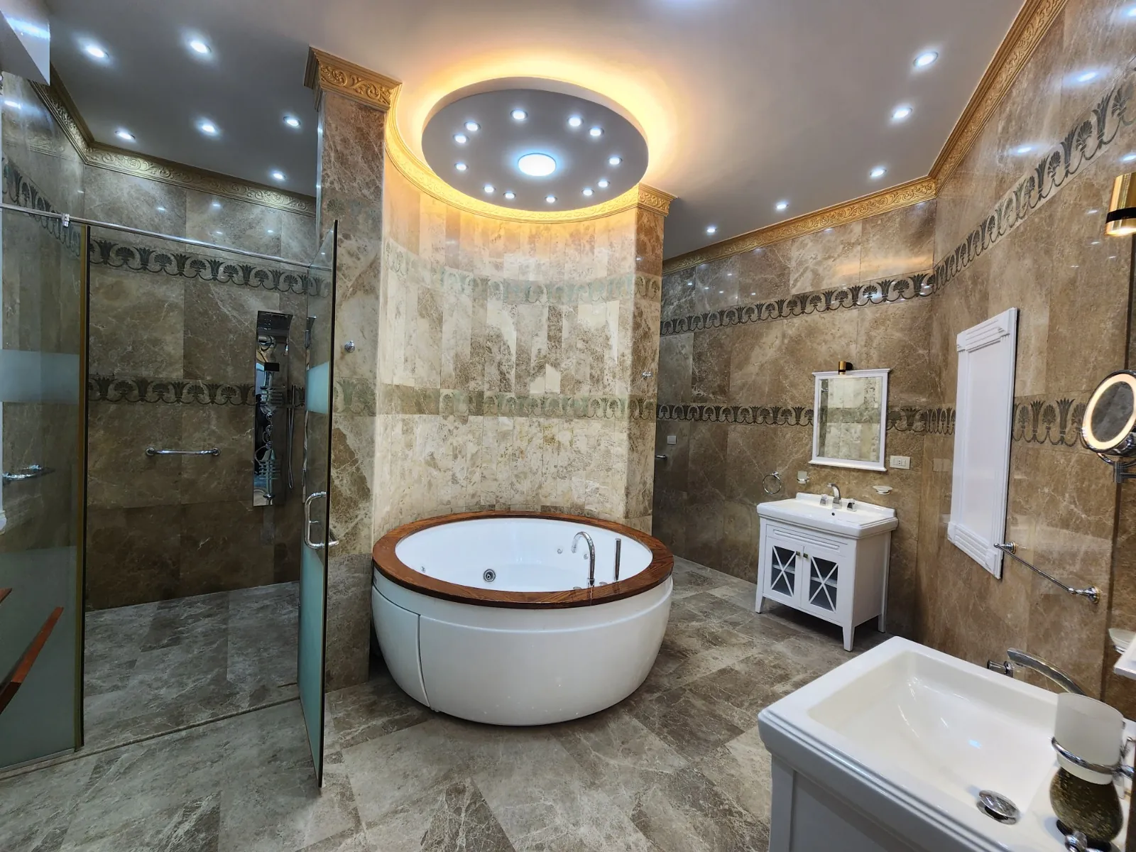A bathroom with stone-patterned surfaces, a round bathtub and circular ceiling lighting